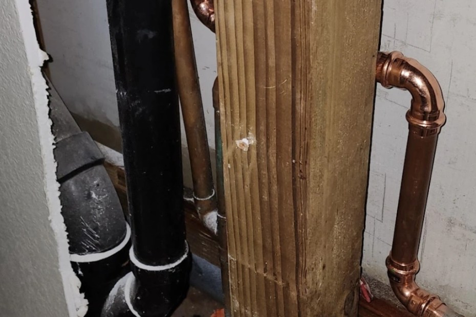 Black ABS drain pipe and fittings beside new copper supply lines in an opened wall next to a wood post