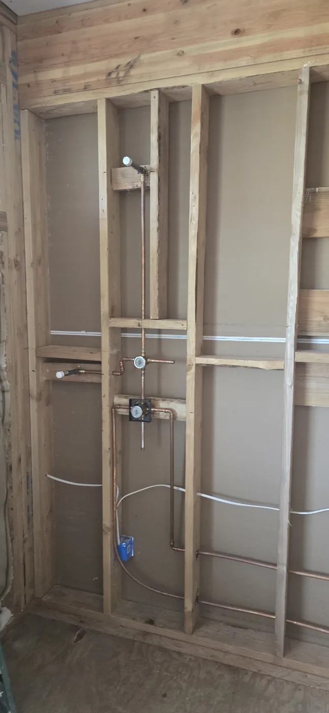 New copper supply lines and a shower valve rough-in running through an open framed wall, with white lines along the studs