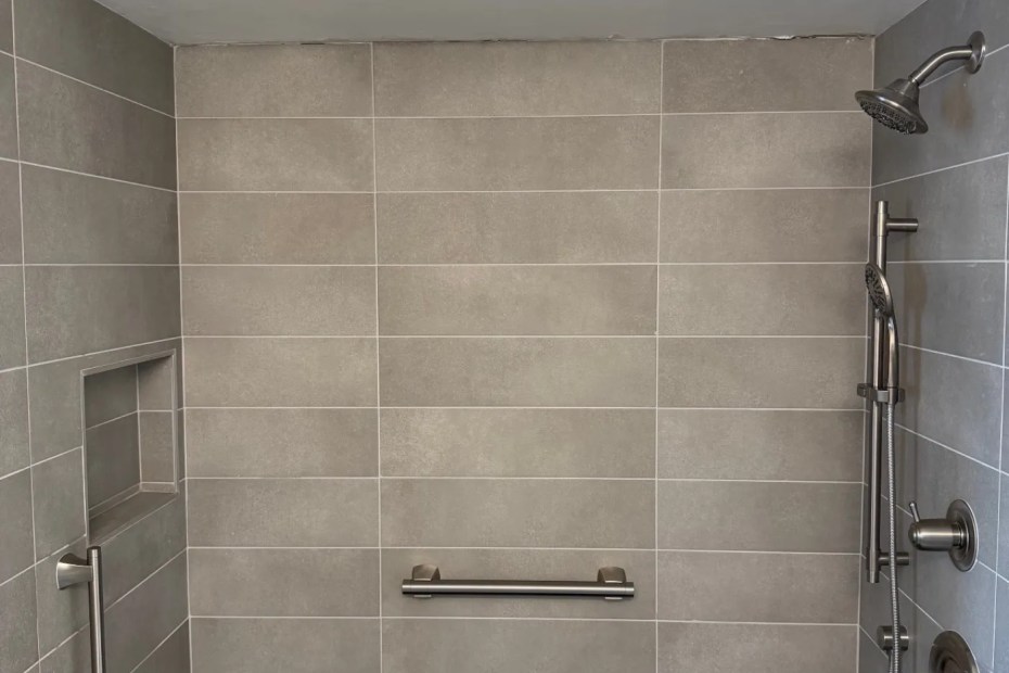 Finished walk-in shower in tan large-format tile with a chrome grab bar and hand shower