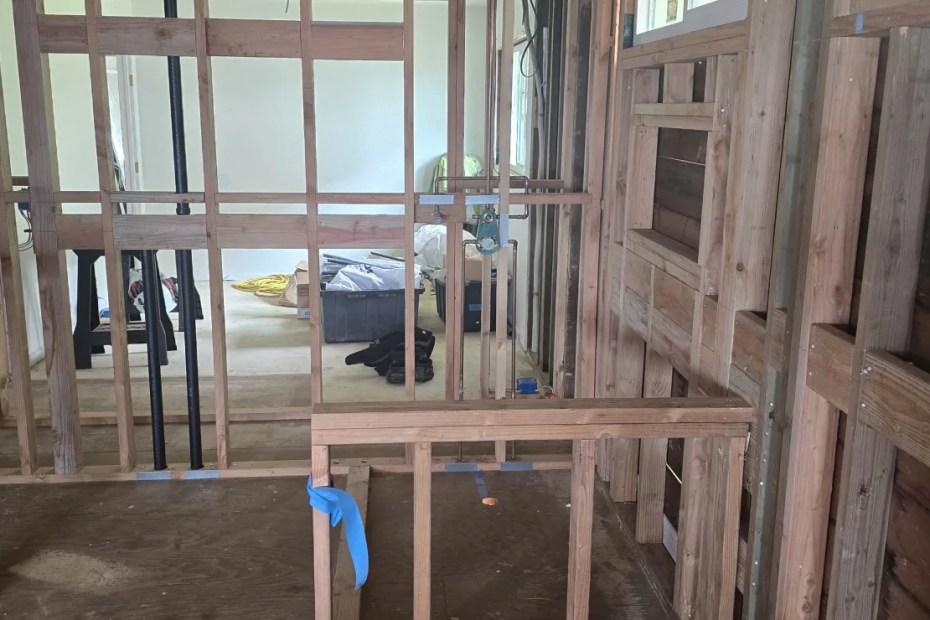 Interior wood framing of a new build with bare studs and blocking and daylight through the openings